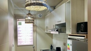Een compacte keuken met een gasfornuis, een spoelbak, een magnetron en een Hisense koelkast. Boven het fornuis hangt een decoratieve geweven lamp.