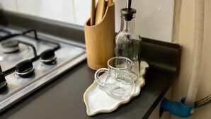 Een aanrecht met een gasfornuis, een houten pannenrek, een glazen fles en een kleine glazen karaf.