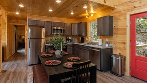 A wooden cabin interior with a kitchen, dining area, and a red door. - Crimson Landing l Lux Cabin in RRG, Dome, Hot Tub (Stanton)