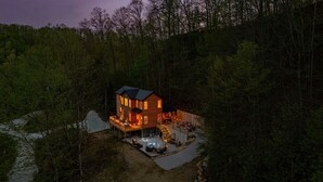 A two-story wooden cabin with a deck, surrounded by forest. - Crimson Landing l Lux Cabin in RRG, Dome, Hot Tub (Stanton)