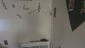 Quarto com ar-condicionado fixado na parede, parede decorada com uma frase, e um par de sapatos no chão.