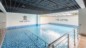 Una piscina interior con suelo de baldosas, barandillas de metal y paredes con la marca 'THE LOFTEL'.