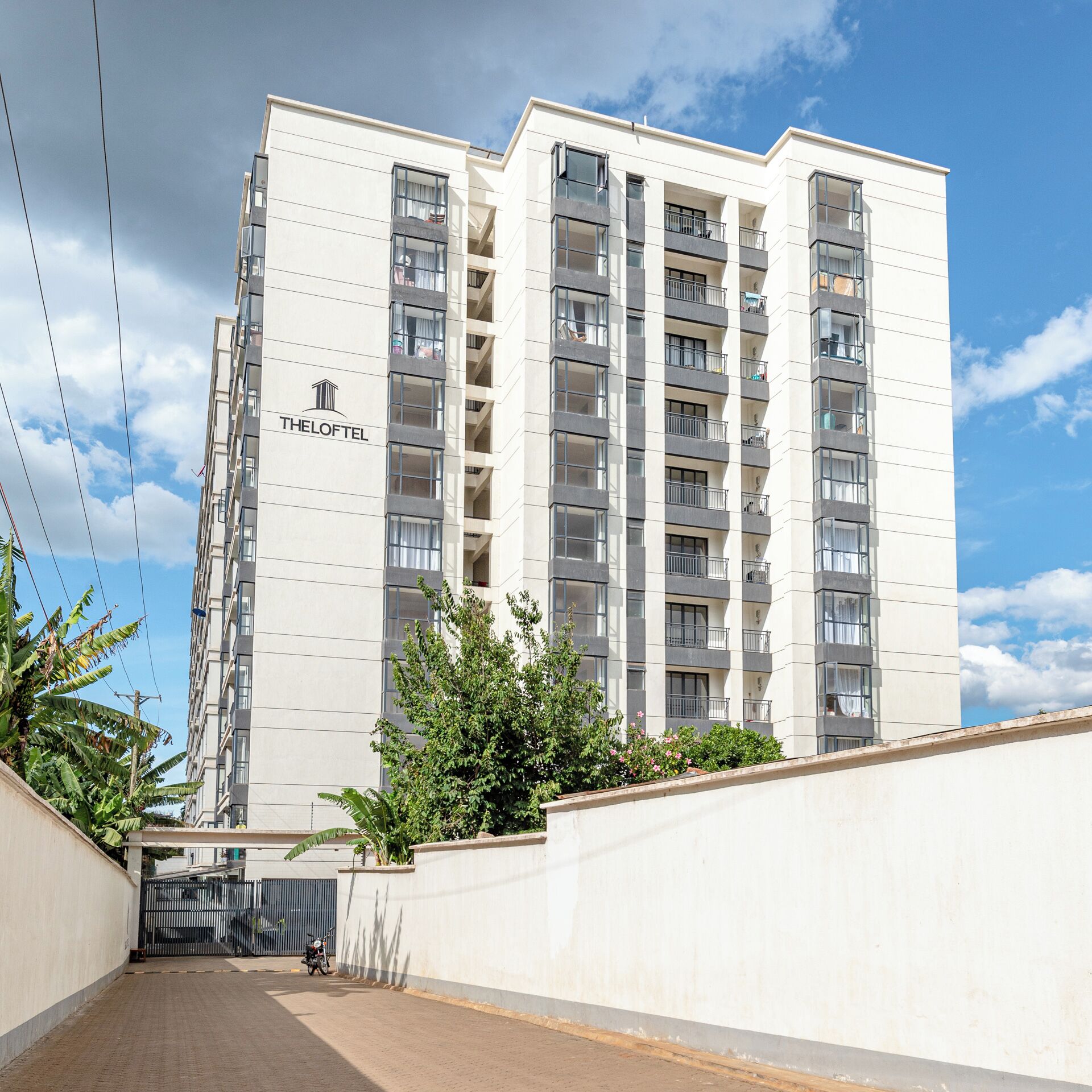 A multi-story hotel building with balconies, a gated entrance, and a clear sky.
