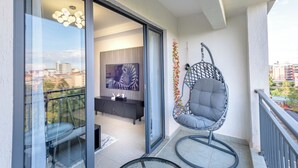 Een balkon met een glazen deur, een hangstoel, een eettafel en een schilderij.
