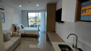 Een compacte hotelkamer met een bed, een sofa, een kleine kitchenette en een balkon met uitzicht.