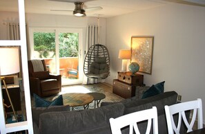 A living room with a sofa, armchair, and a hanging chair. There is a table with a lamp, a globe, and a painting on the wall.