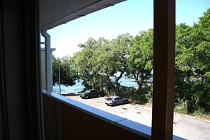 A view from a window overlooking a parking area with two cars, trees, and a body of water.
