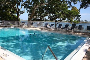A swimming pool with lounge chairs, a metal fence, and trees in the background.