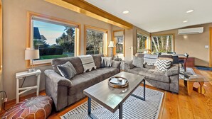 A spacious living room with two sofas, a coffee table, and large windows. - Steps to the Beach: Arch Cape Cozy Cottage w Sauna (Arch Cape)