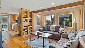 A modern living room with a sofa, coffee table, and built-in shelving. - Steps to the Beach: Arch Cape Cozy Cottage w Sauna (Arch Cape)