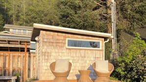 A wooden building with a sign, two wicker chairs, and a small table. - Steps to the Beach: Arch Cape Cozy Cottage w Sauna (Arch Cape)