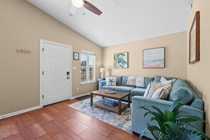 A living room with a sofa, coffee table, and a ceiling fan. - New! • Sunset Palms • 2BR • 5 Min Walk to Beach! (Panama City Beach)