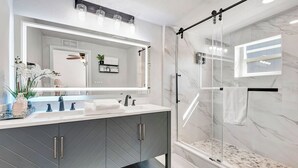 A modern bathroom with a large mirror, two sinks, a shower with glass doors, and marble walls. - Cozy 1-bedroom house with AC in delightful North Port (North Port)