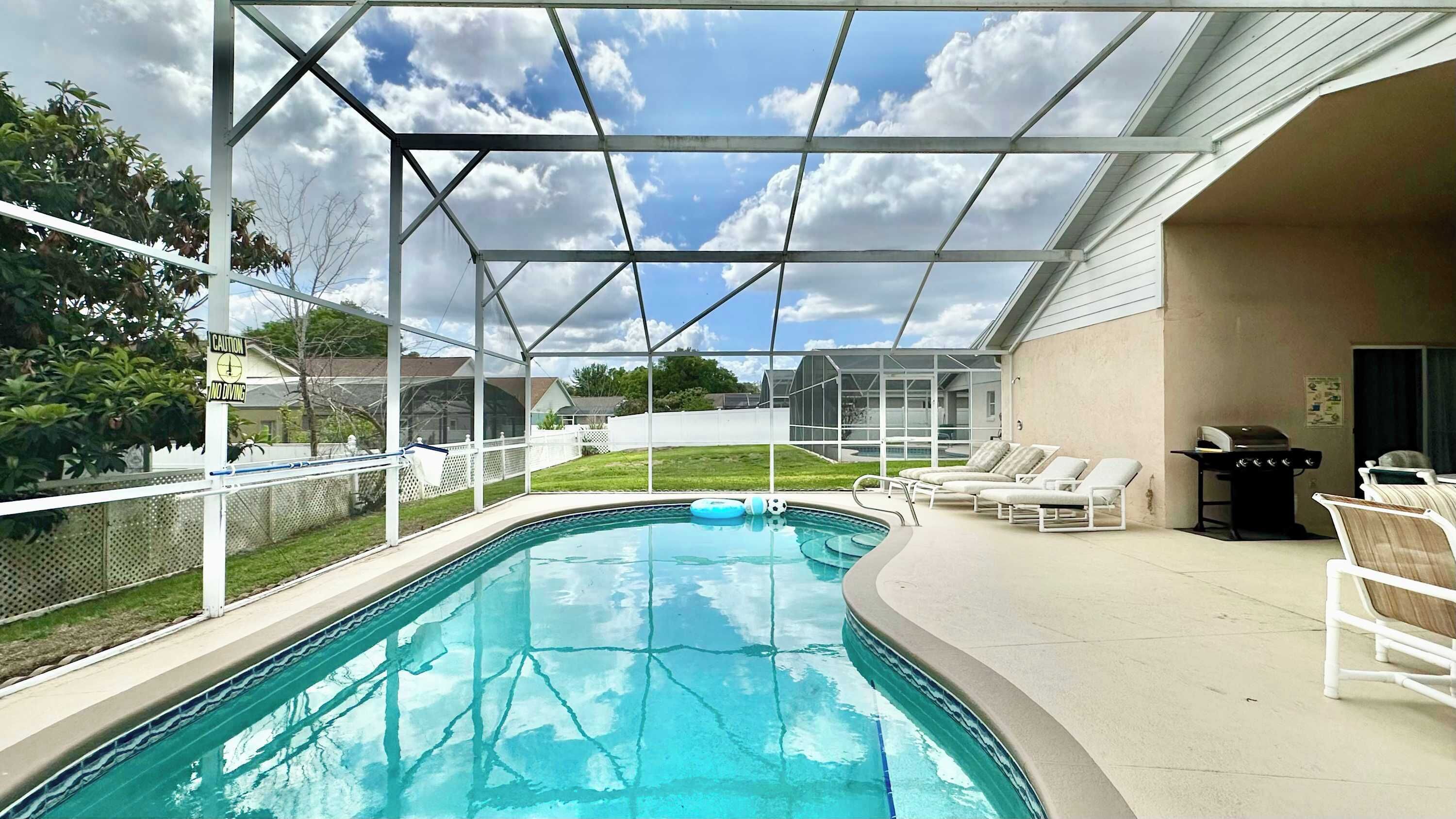 A swimming pool with a covered area, lounge chairs, and a barbecue grill.