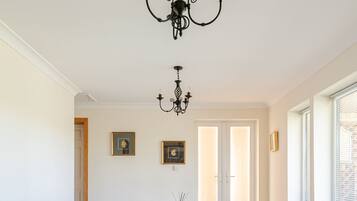 A dining room with a white table, four upholstered chairs, a black chandelier, and framed pictures on the walls.