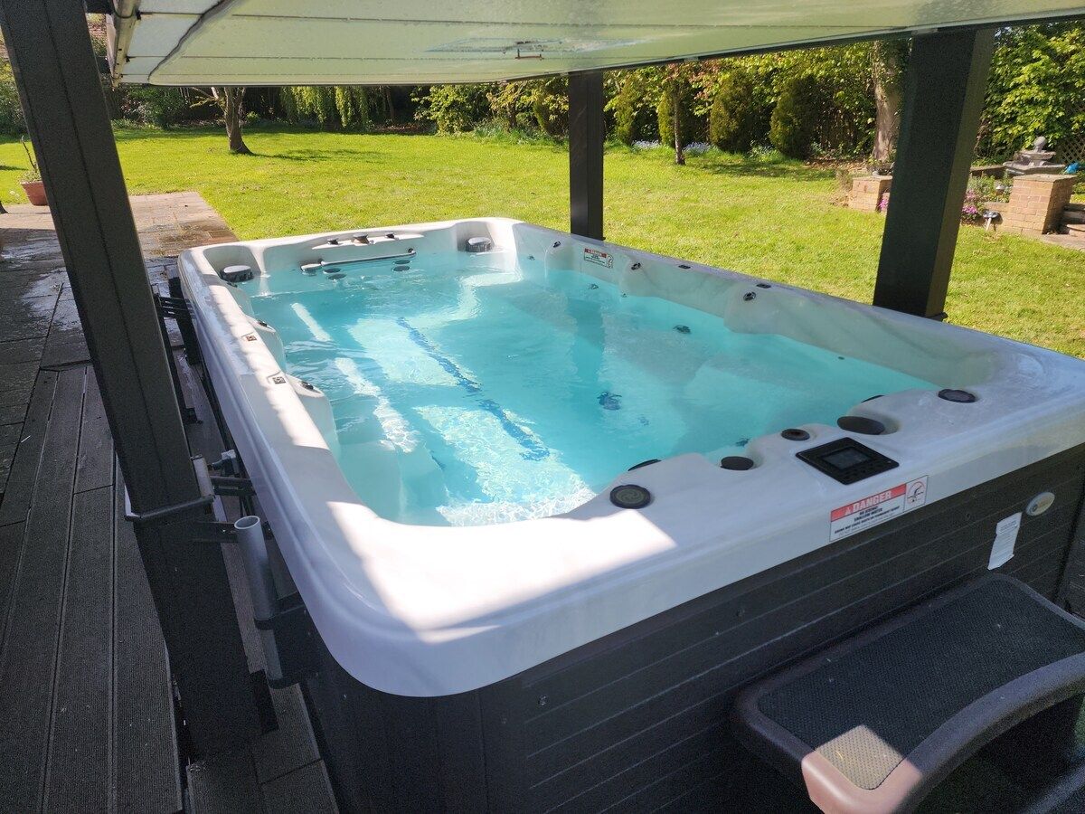 A hot tub with a safety warning label, set on a wooden deck with a grassy yard in the background.