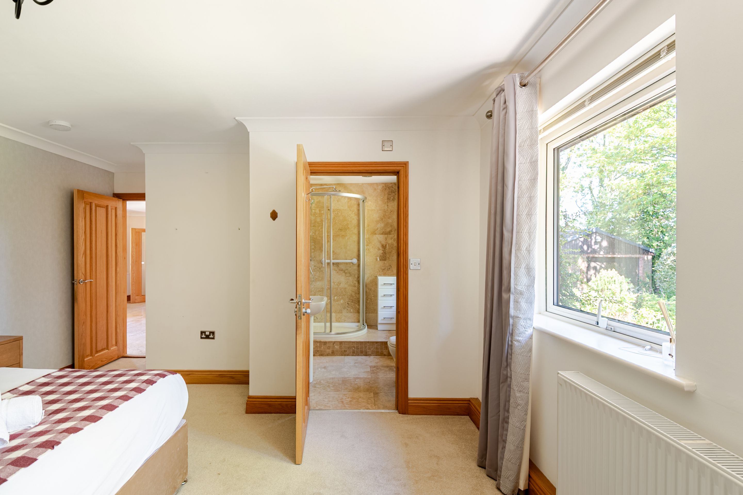 Ein Schlafzimmer mit Bett, einem Fenster mit Vorhängen sowie einem Badezimmer mit Dusche und Toilette.