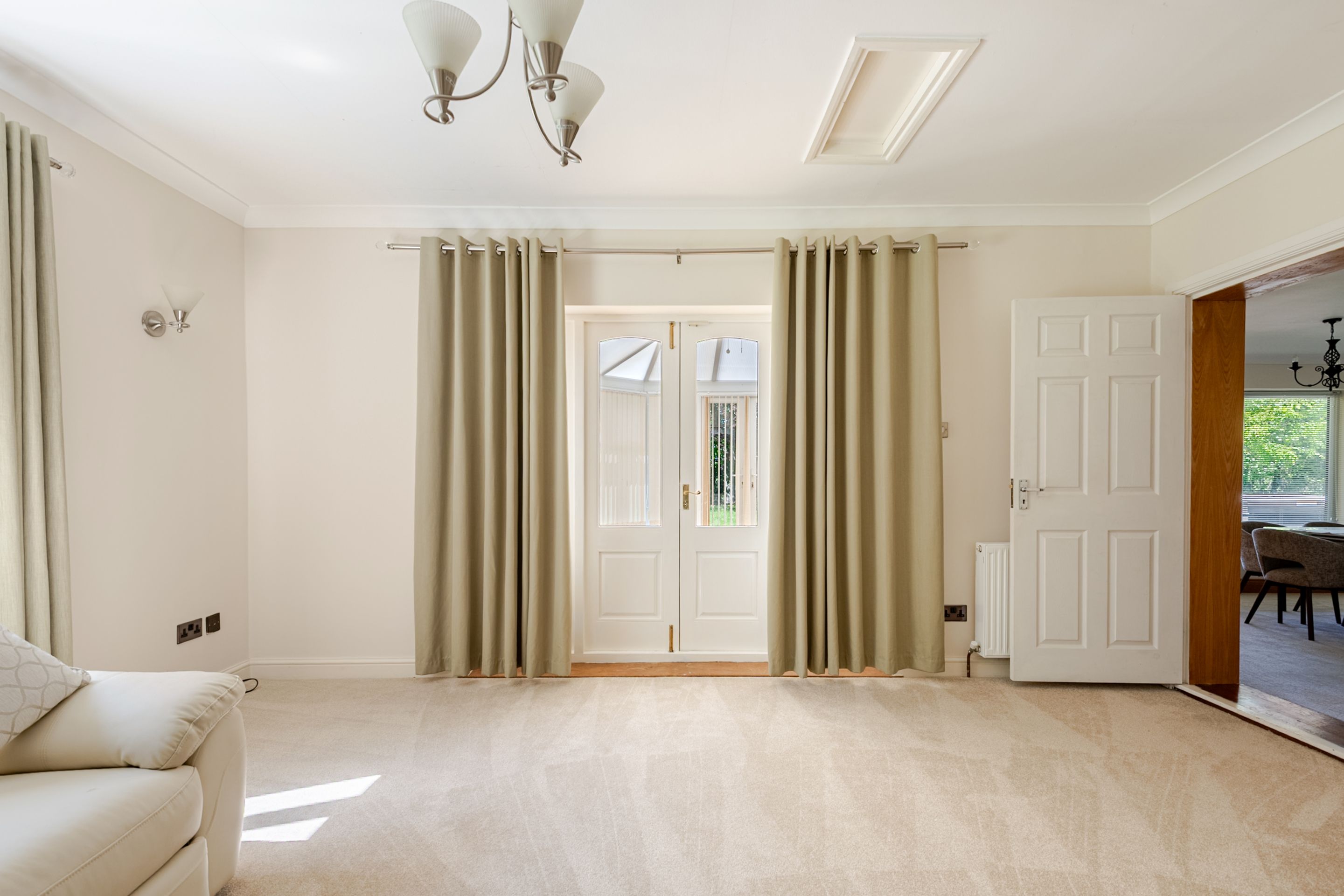 A spacious room with a large door, beige curtains, a light fixture, and a radiator.