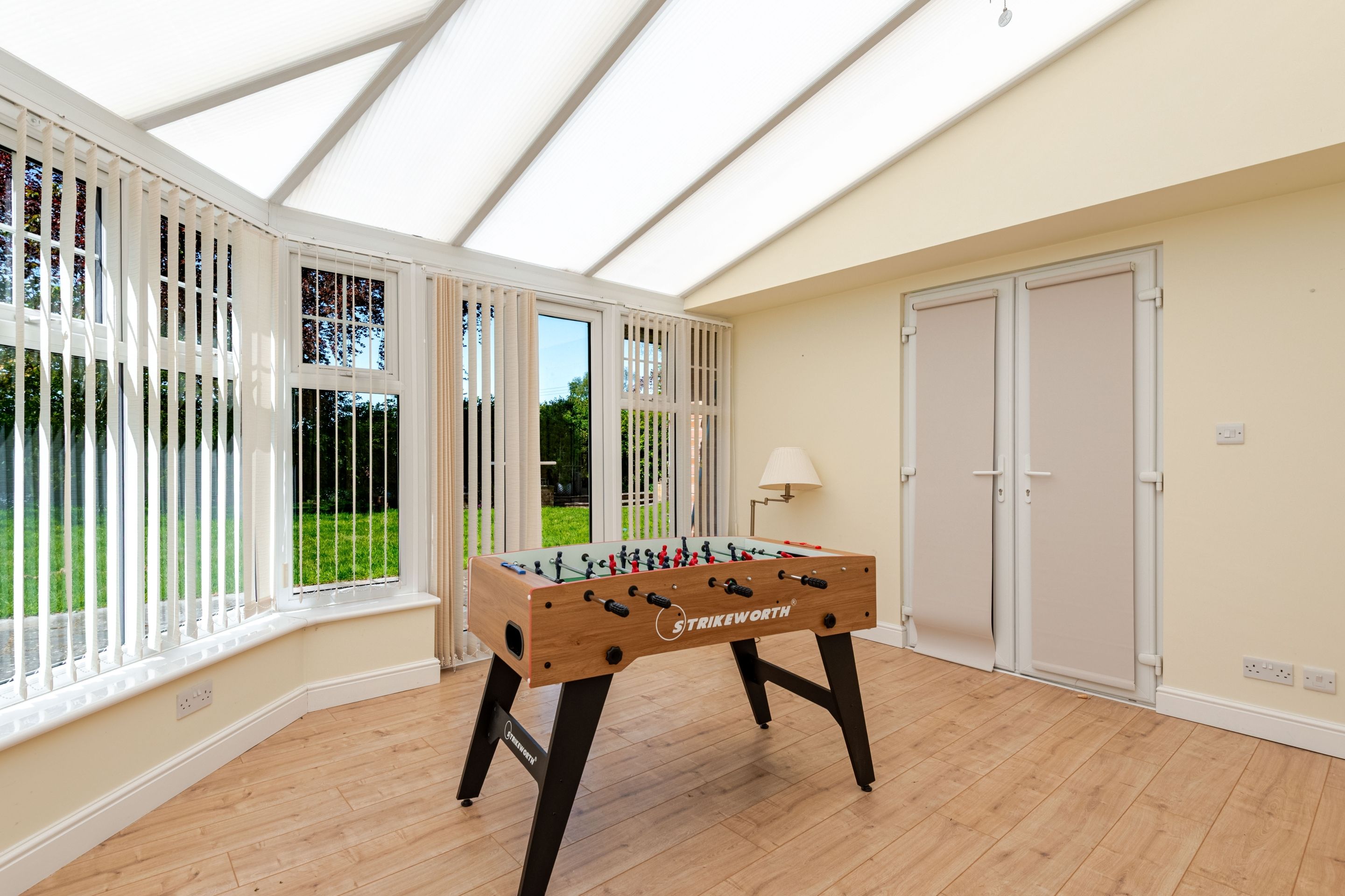 A room with a foosball table, a door, and a window with a view of greenery.
