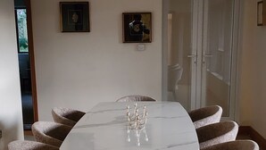 Un comedor con una mesa de mármol, seis sillas tapizadas, una araña y cuadros enmarcados en la pared.