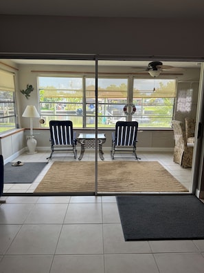 A room with a sliding glass door leading to a balcony, two chairs, a small table, a lamp, and a decorative sign. - Quiet Canal in Ruskin on Little Manatee River with boat access (Ruskin)