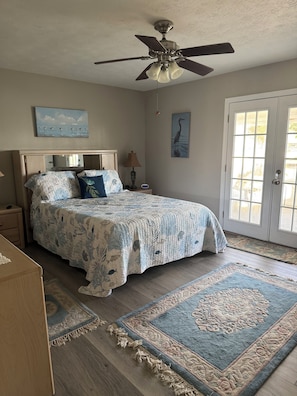 A bedroom with a bed, a ceiling fan, a nightstand, a lamp, a painting, and a door. - Quiet Canal in Ruskin on Little Manatee River with boat access (Ruskin)