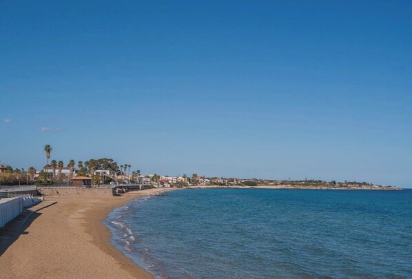 A beach with a clear sky, a sandy shore, and buildings in the background. - The House Of Egizia (Avola)