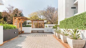 Patio moderno all'aperto con pergola in legno, piante in vaso e vialetto lastricato.