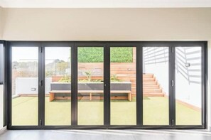 Un interior moderno con una puerta de cristal corredera que da a un espacio exterior con una banca y escalones.