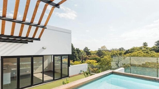 Un edificio moderno con piscina, ampie vetrate e una pergola in legno.