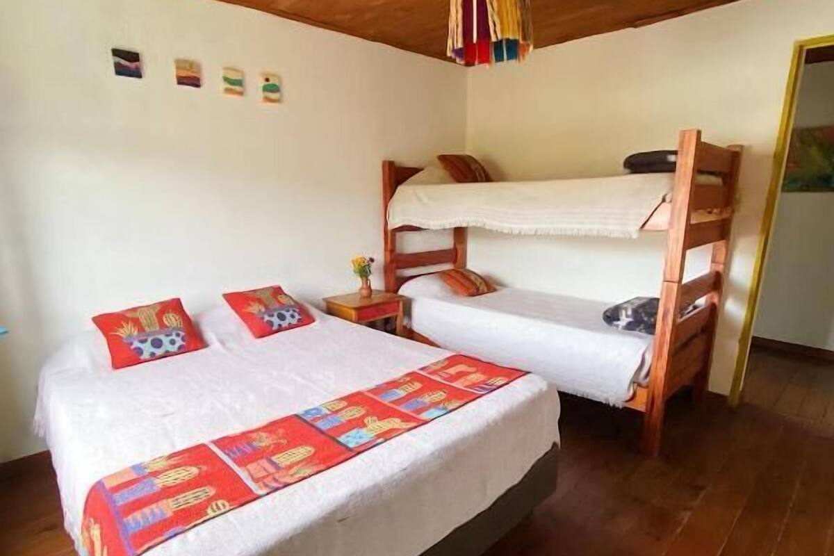 Ein Zimmer mit Etagenbett, einem Einzelbett mit farbenfroher Bettwäsche, einer Holzbalkendecke und einem kleinen Teppichboden.