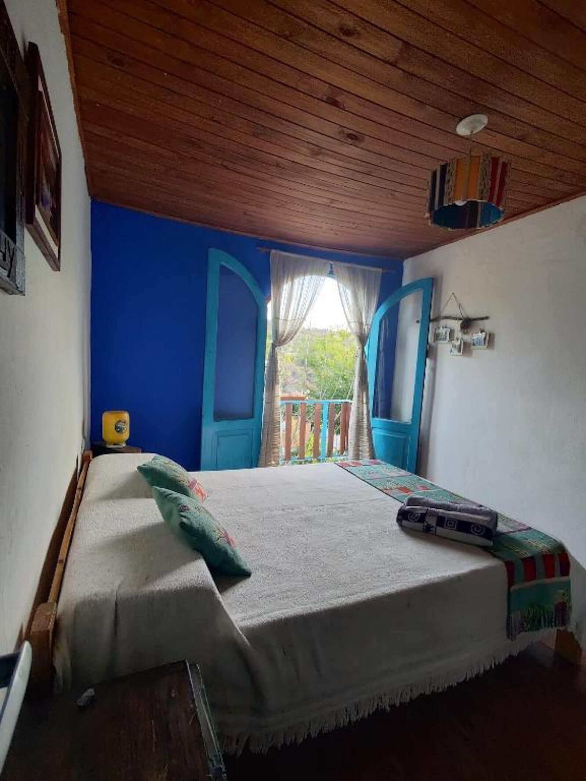 A room with a bed, a window with curtains, a ceiling fan, and a view of greenery outside.