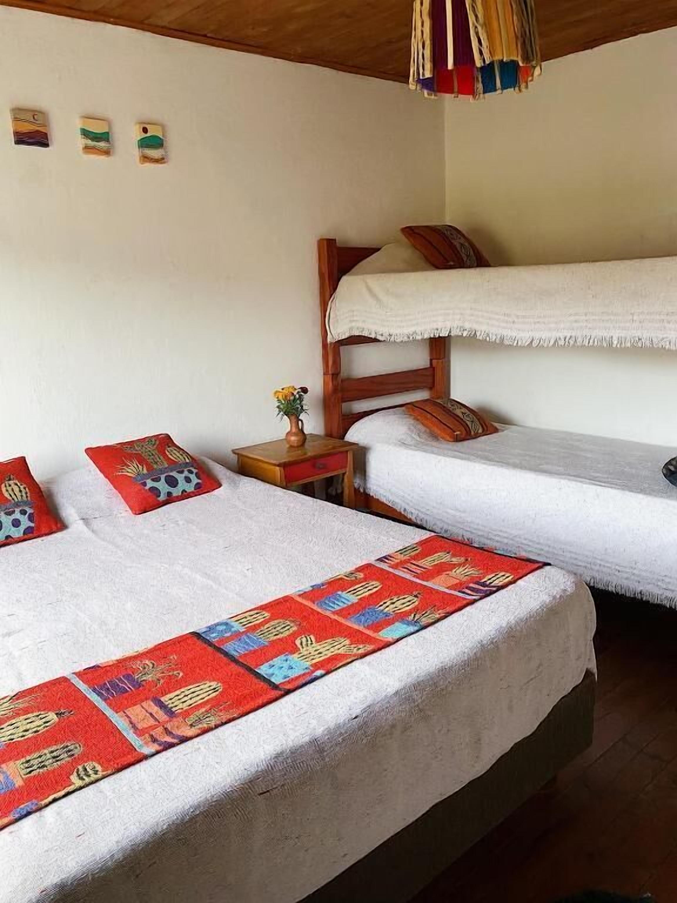 A room with two beds, a small table with a vase, and a wooden headboard.