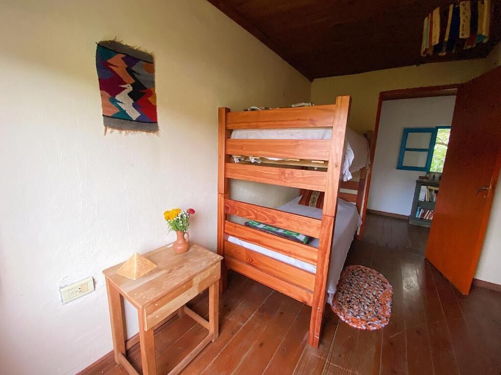 A bunk bed with a wooden frame, a small wooden table with a vase of flowers, and a patterned rug on the floor.