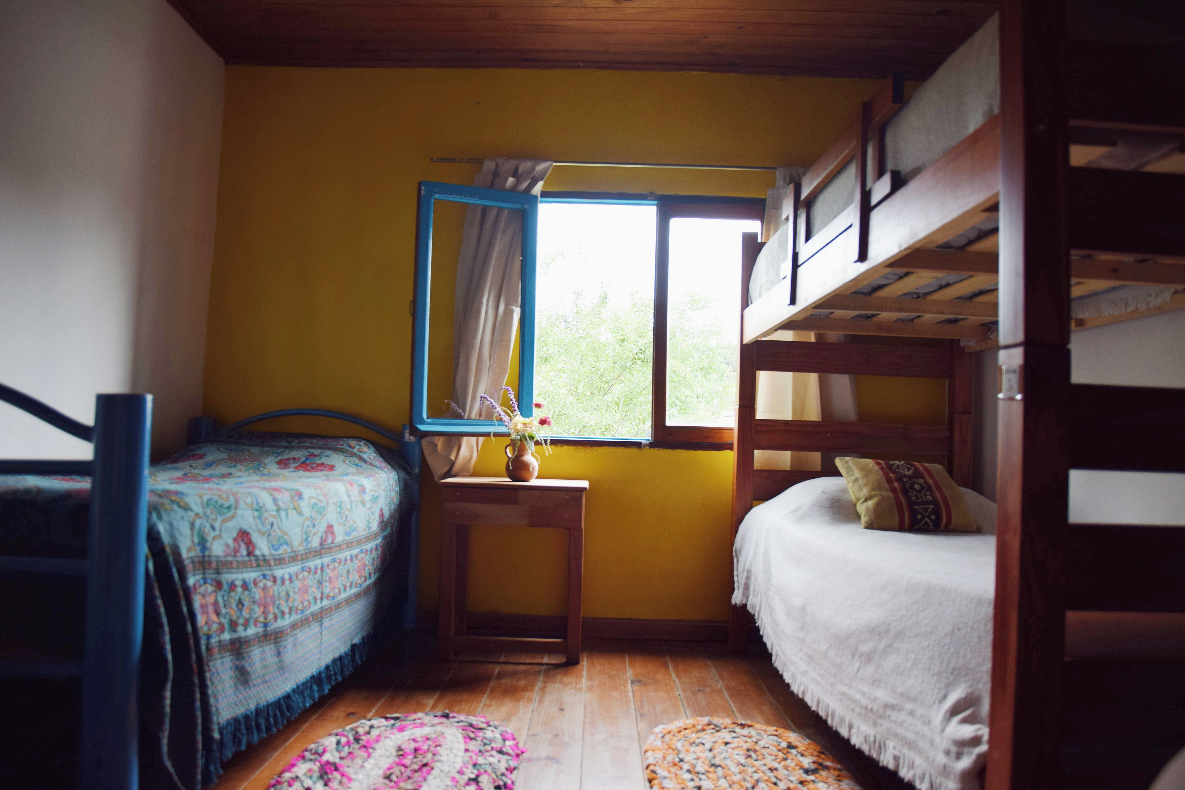 Een kleine, gezellige kamer met twee bedden, een raam met gordijnen en een houten stapelbed.