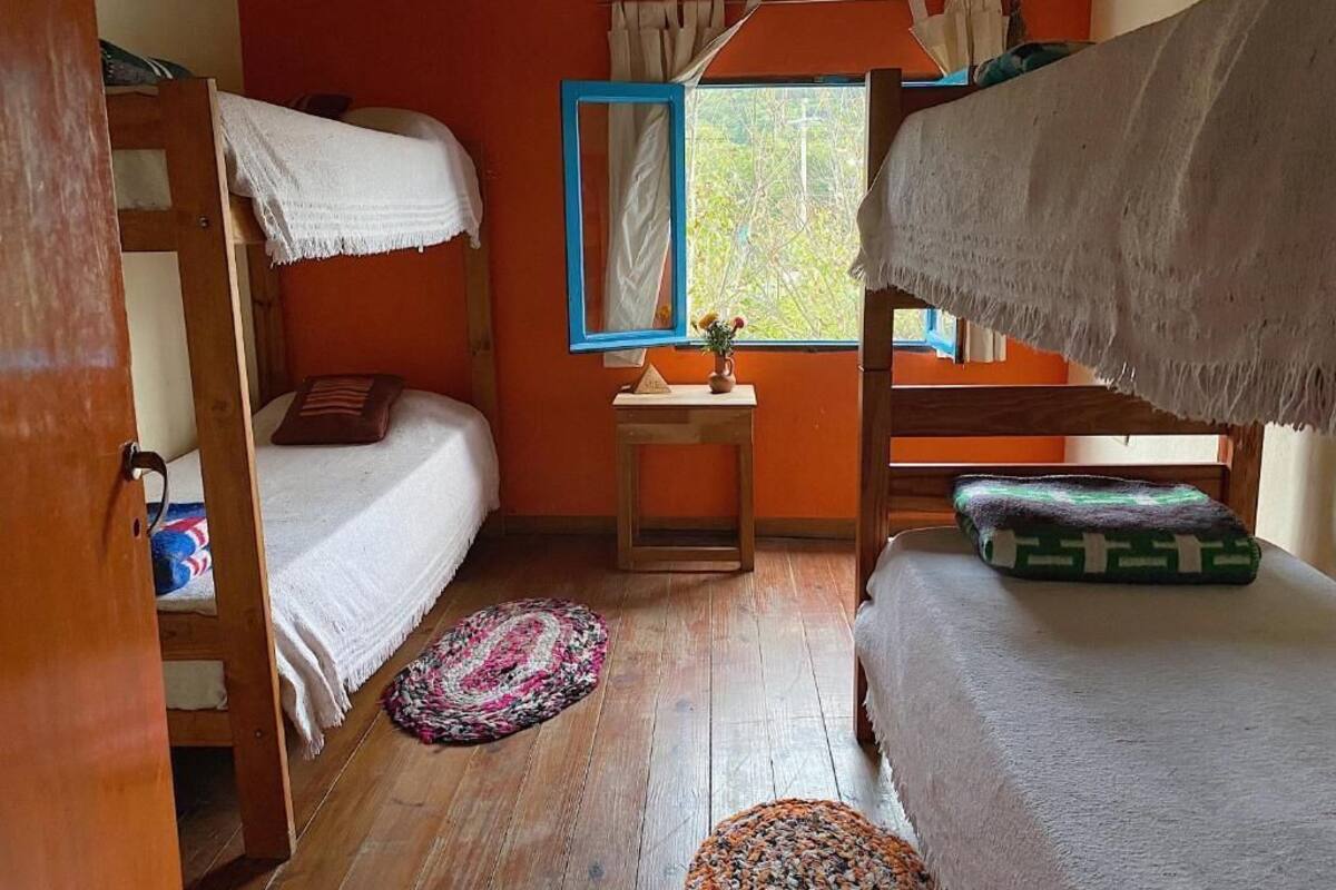 Ein Zimmer mit Etagenbetten, einem kleinen Tisch mit einer Vase und einem Fenster mit Vorhängen.