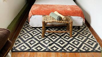 Un dormitorio con una cama, una lámpara colgante, un estante con plantas en la pared y una alfombra estampada.