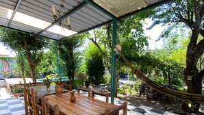 A checkered outdoor dining area with a covered roof, wooden table and chairs, and a hammock.