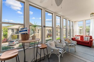Una habitación luminosa con ventanas grandes, muebles de mimbre, un sofá rojo y vistas a casas vecinas.