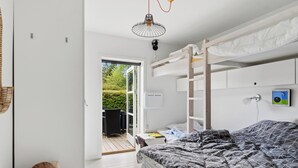 A bunk bed room with a door leading to an outdoor area, a small table, and a wall-mounted light fixture. - Cozy cottage in Nykøbing Sjælland (Nykøbing Sj)