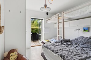 A bunk bed room with a door leading to an outdoor area, a small table, and a wall-mounted light fixture. - Cozy cottage in Nykøbing Sjælland (Nykøbing Sj)