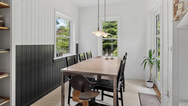 A dining area with a wooden table, black chairs, pendant lights, and a potted plant. - Cozy cottage in Nykøbing Sjælland (Nykøbing Sj)