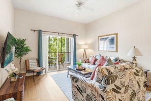 A living room with a sofa, a coffee table, a TV, a plant, and a sliding glass door leading to a balcony. - Vacation Dreams at Bahama Bay (Davenport)