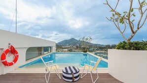 A pool with two lounge chairs and a striped ottoman, a lifebuoy, and a view of a mountain. - Sunset View Condo Steps from Karon Beach #C162 (Tambon Karon)