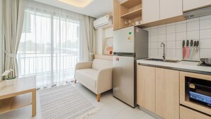 A compact living space with a kitchenette, a sofa, a dining table, and a large window with sheer curtains. - Sunset View Condo Steps from Karon Beach #C162 (Tambon Karon)