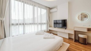 A hotel room with a bed, a TV, a desk, a mirror, and a window with curtains. - Sunset View Condo Steps from Karon Beach #C162 (Tambon Karon)