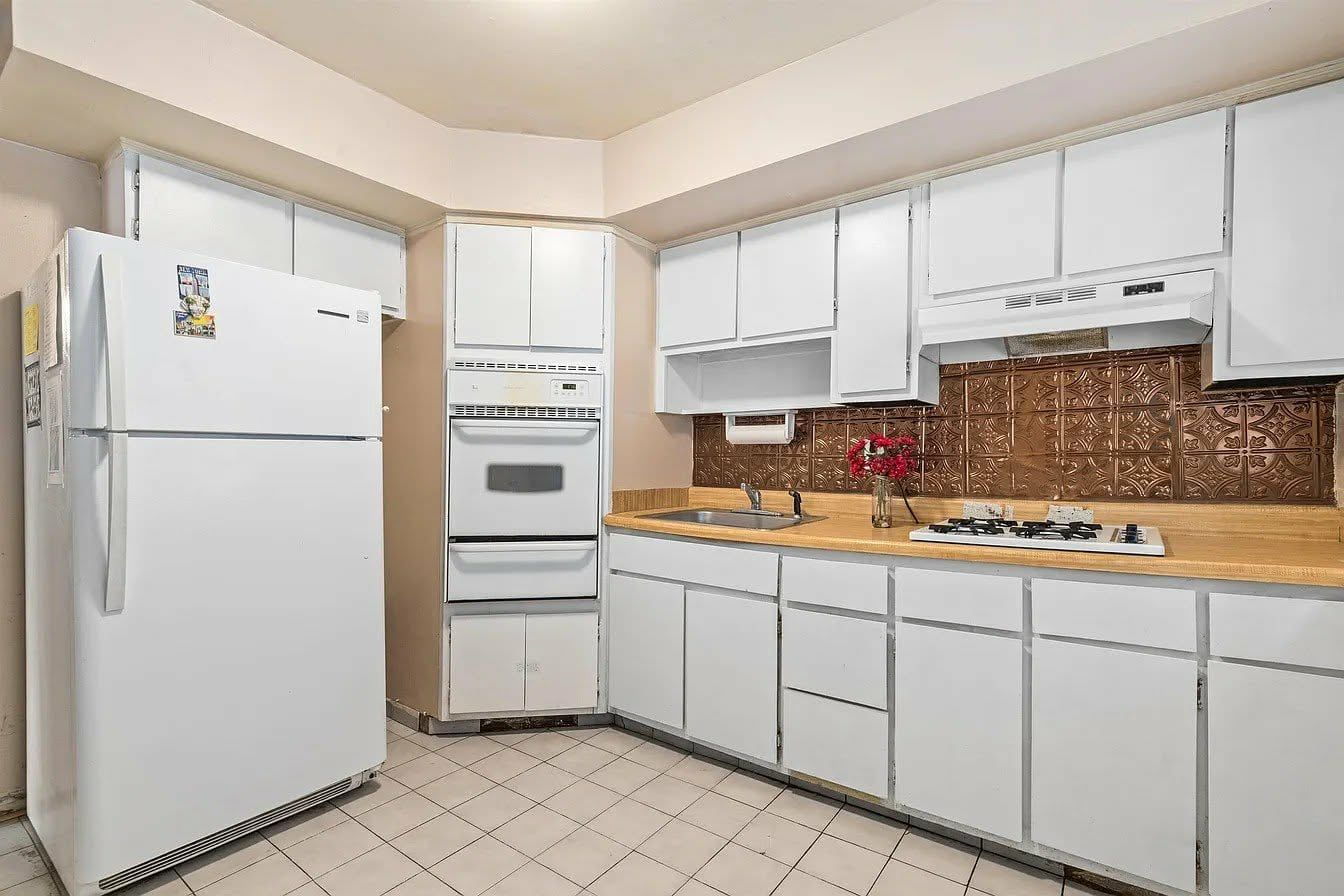 A kitchen with white cabinets, a refrigerator, an oven, a sink, and a stove.