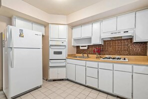 Una cocina con armarios blancos, un refrigerador, un horno, un lavamanos y una estufa.