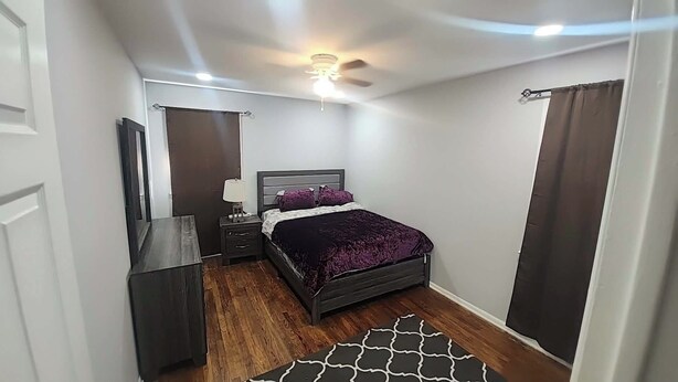 A bedroom with a bed, bedside table, lamp, and a ceiling fan.