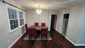 A dining area with a round table, red chairs, a chandelier, and a window with blinds.